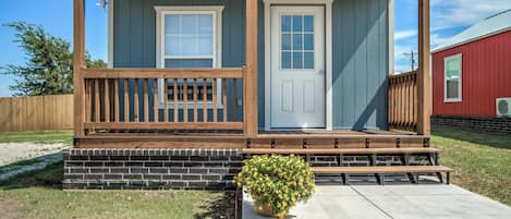 A small house with a porch, two doors, a small garden, and a gravel driveway.
