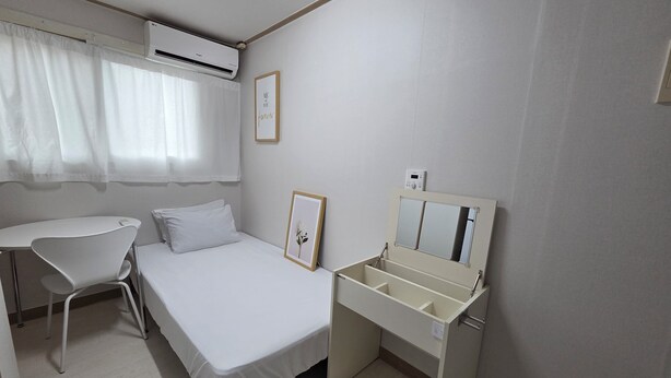 Ett kompakt hotellrum med en säng, ett skrivbord, en stol och en liten sminkbord med spegel.