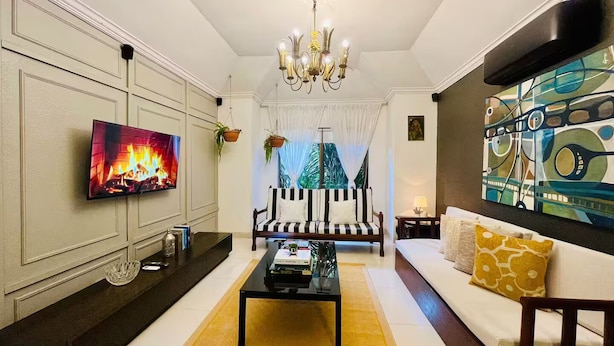 A living room with a flat-screen TV, a chandelier, a sofa, a coffee table, and a painting on the wall.