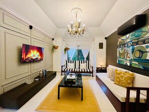Una sala de estar con una televisión de pantalla plana, un candelabro, un sofá, una mesa de centro y un cuadro en la pared.