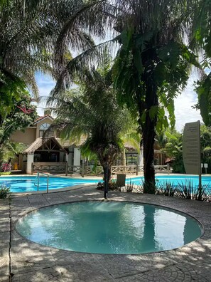 A pool area with a palm tree, a thatched-roof structure, and a sign with text. - Dúplex Premium - Piscinas, Jacuzzi & Sauna (Santa Cruz de la Sierra)