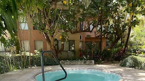 A hot tub with steps leading into it, surrounded by greenery and a building in the background. - Dúplex Premium - Piscinas, Jacuzzi & Sauna (Santa Cruz de la Sierra)