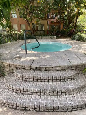 A hot tub with steps leading into it, surrounded by greenery and a building in the background. - Dúplex Premium - Piscinas, Jacuzzi & Sauna (Santa Cruz de la Sierra)