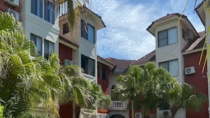 A residential building with a central entrance, surrounded by palm trees and a parked car.
