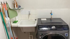 A laundry room with a washing machine, a sink, and various cleaning tools.