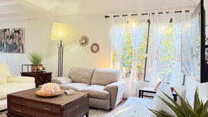 A living room with a sofa, a coffee table, a lamp, and a view of greenery through sheer curtains.