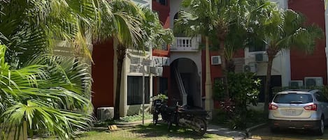 A residential building with a central entrance, surrounded by palm trees and a parked car.