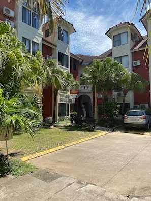 A residential building with a central entrance, surrounded by palm trees and a parked car.