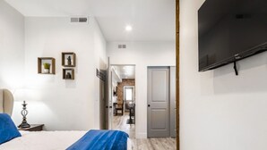 Una camera da letto con un letto, una TV a muro e un corridoio che conduce a una sala da pranzo.