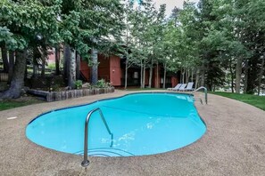 A swimming pool with a metal ladder, surrounded by trees and a building with a red facade. - 4BR Canyon Lodge Base - Shuttle, Hot Tub & Room for 10 (Mammoth Lakes)