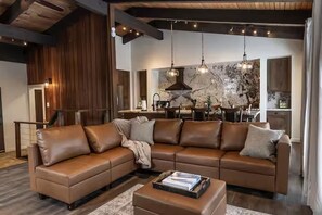 A modern living room with a sectional sofa, a coffee table, and a kitchen in the background. - 4BR Canyon Lodge Base - Shuttle, Hot Tub & Room for 10 (Mammoth Lakes)