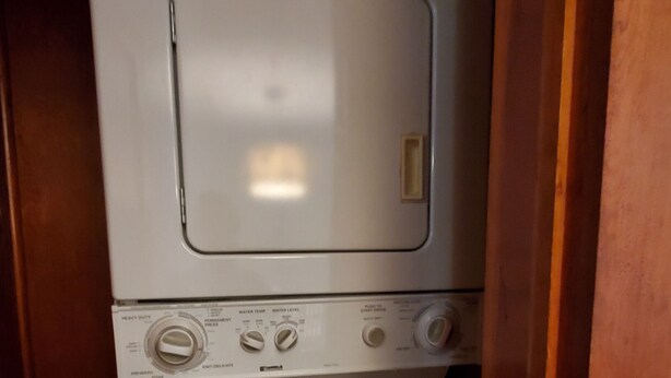 A stacked washer and dryer unit with control knobs and a door. - Goodyear Lake Boathouse - charming historic cottage overlooking the water (Oneonta)