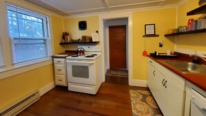 A kitchen with a stove, sink, and window with blinds. - Goodyear Lake Boathouse - charming historic cottage overlooking the water (Oneonta)
