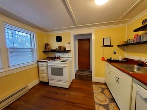 A kitchen with a stove, sink, and window with blinds. - Goodyear Lake Boathouse - charming historic cottage overlooking the water (Oneonta)