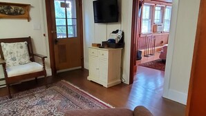 A room with a sofa, a chair, a television, and a wooden door. - Goodyear Lake Boathouse - charming historic cottage overlooking the water (Oneonta)