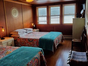 A room with two beds, a desk, a chair, and a window with blinds. - Goodyear Lake Boathouse - charming historic cottage overlooking the water (Oneonta)