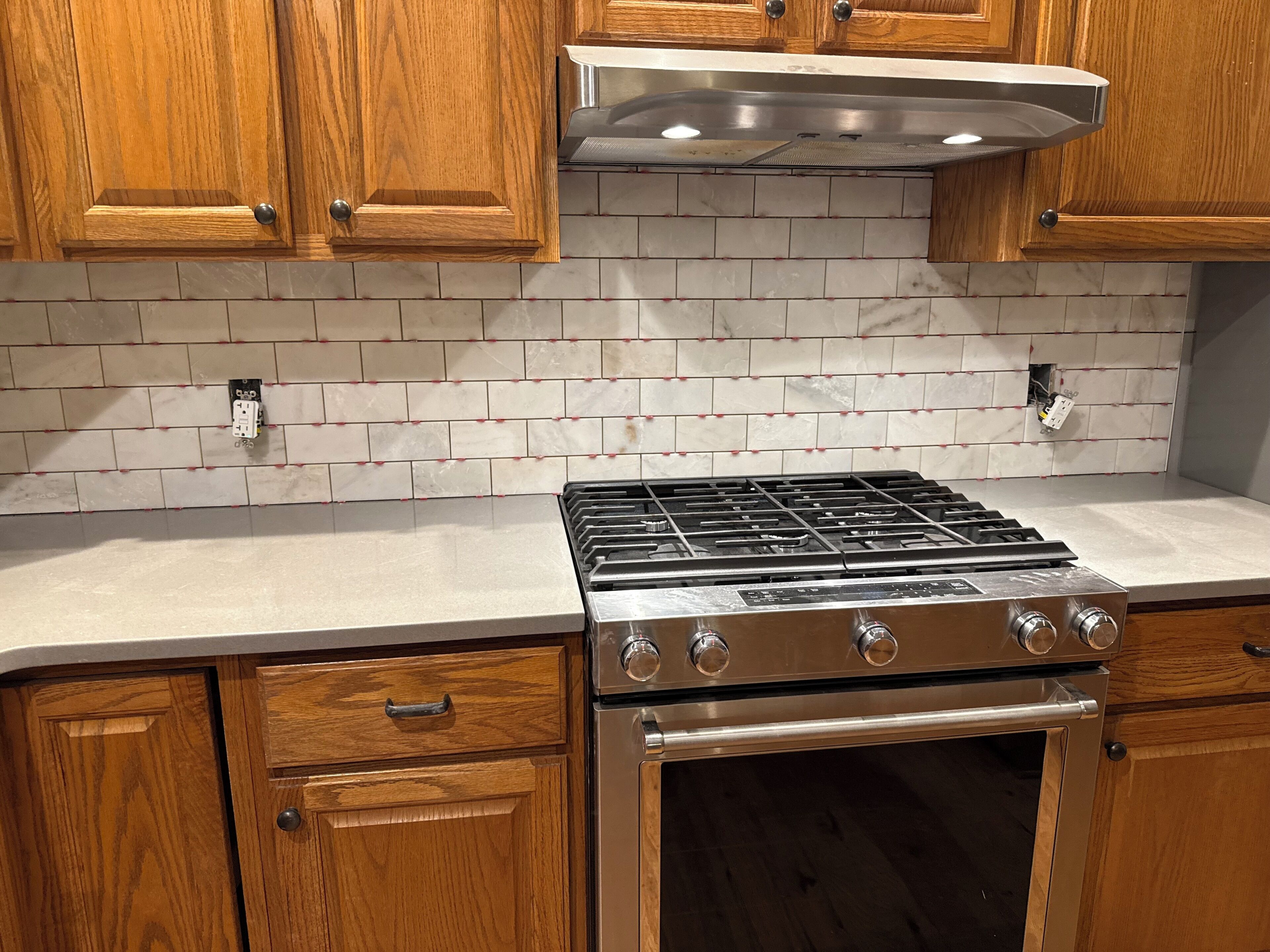 Una cocina con armarios de madera, estufa de acero inoxidable y salpicadero de azulejos.