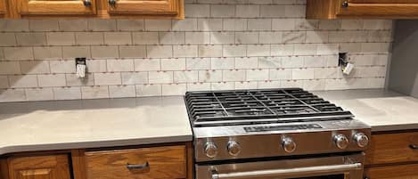 Una cocina con armarios de madera, estufa de acero inoxidable y salpicadero de azulejos.