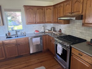 A kitchen with wooden cabinets, a stainless steel range, a dishwasher, and a window with a view of the outdoors.