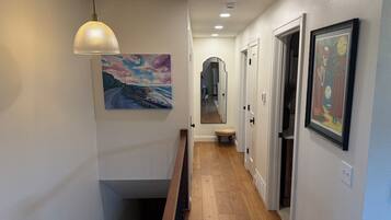 A hallway with wooden flooring, a bench, a pendant light, and framed artwork on the walls.