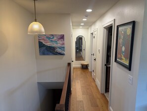 A hallway with wooden flooring, a bench, a pendant light, and framed artwork on the walls.