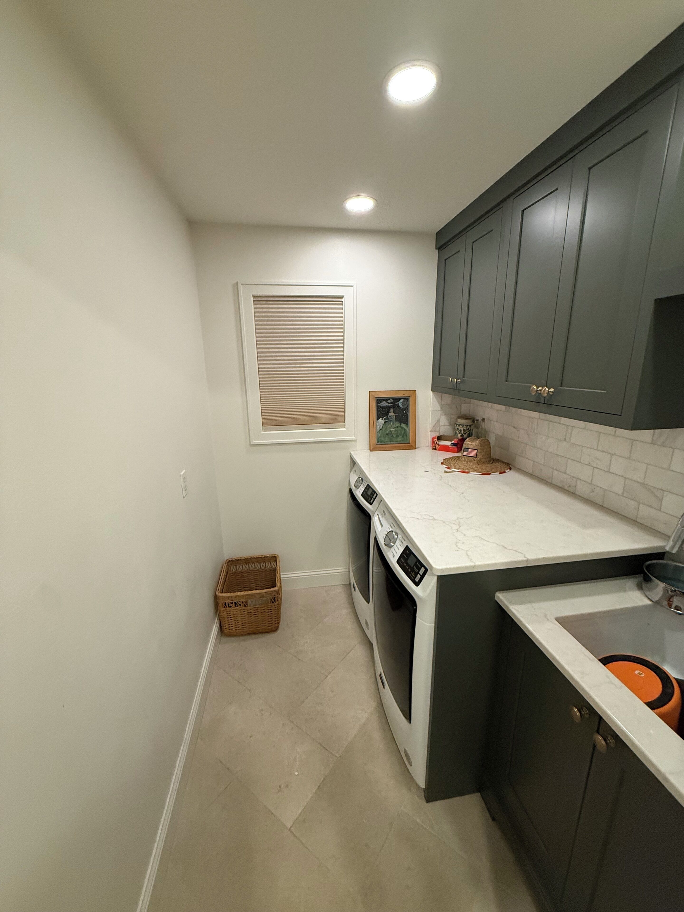 A compact kitchen with built-in appliances, a window with blinds, and a small wicker basket.
