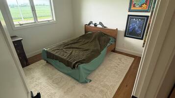 A bedroom with a bed, a window, a door, and a wall with two framed pictures.