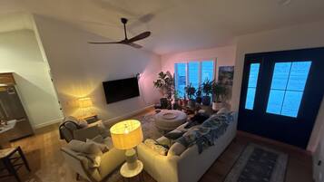 A living room with a sofa, a coffee table, a TV mounted on the wall, and a ceiling fan.