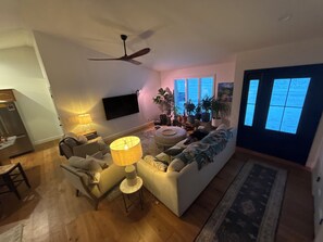 A living room with a sofa, a coffee table, a TV mounted on the wall, and a ceiling fan.