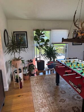 A room with a foosball table, potted plants, and a view through a glass door.