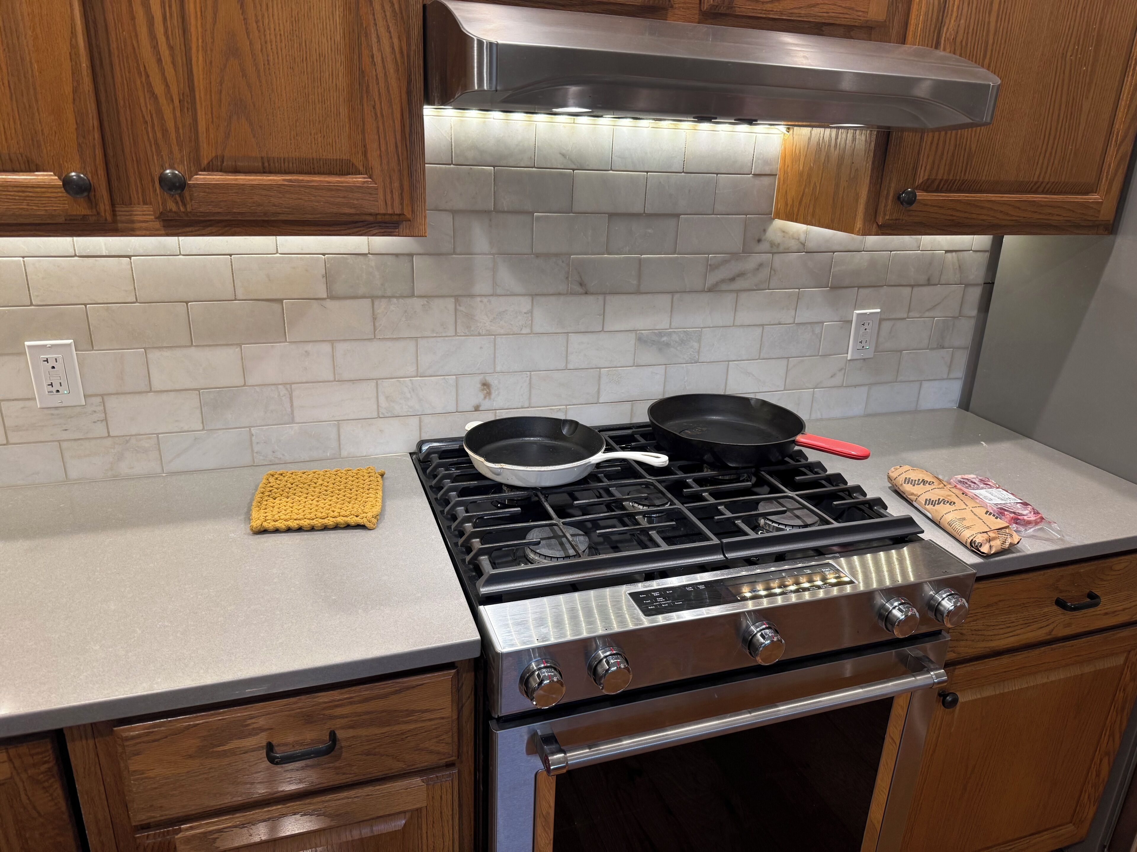 A kitchen with a gas stove, two frying pans, a wooden cutting board, and a stainless steel range hood.