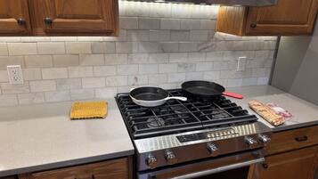 A kitchen with a gas stove, two frying pans, a wooden cutting board, and a stainless steel range hood.