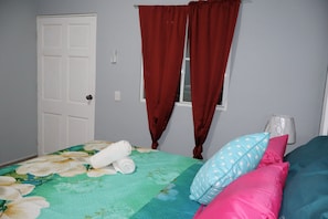 Un dormitorio con cama, ventana con cortinas, puerta y mesita de noche con lámpara.