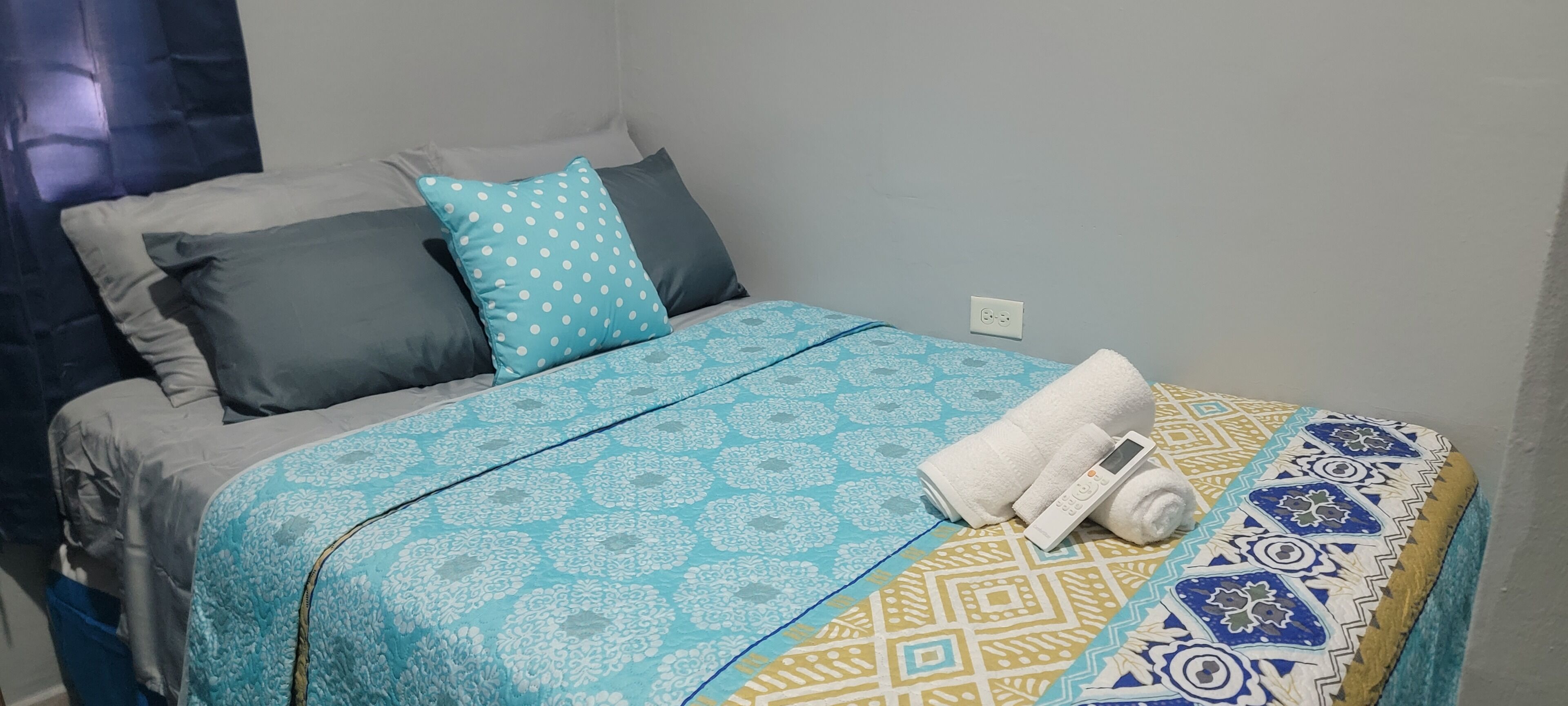 Een net opgemaakt bed met een beddekleed met patroon, kussens en een opgerolde handdoek.