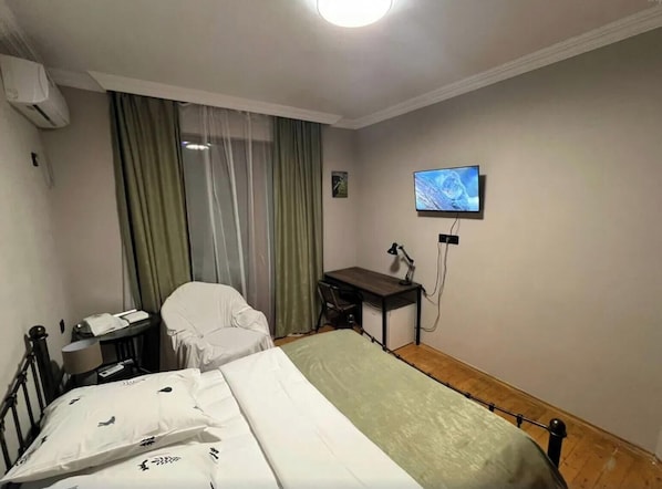 Habitación de hotel con cama, escritorio, silla, aire acondicionado, televisor y ventana con cortinas.