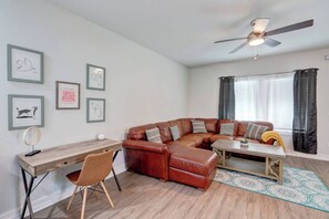 A living room with a brown leather sofa, a wooden coffee table, a desk with a chair, and a ceiling fan. - ↬Picasso`s Bungalow Triple King Beds Nxt ② Dwntwn↫ (Tampa)