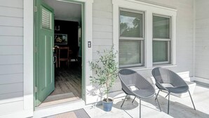 L'ingresso di una casa con una porta verde, due finestre, una pianta in vaso e due sedie all'esterno.