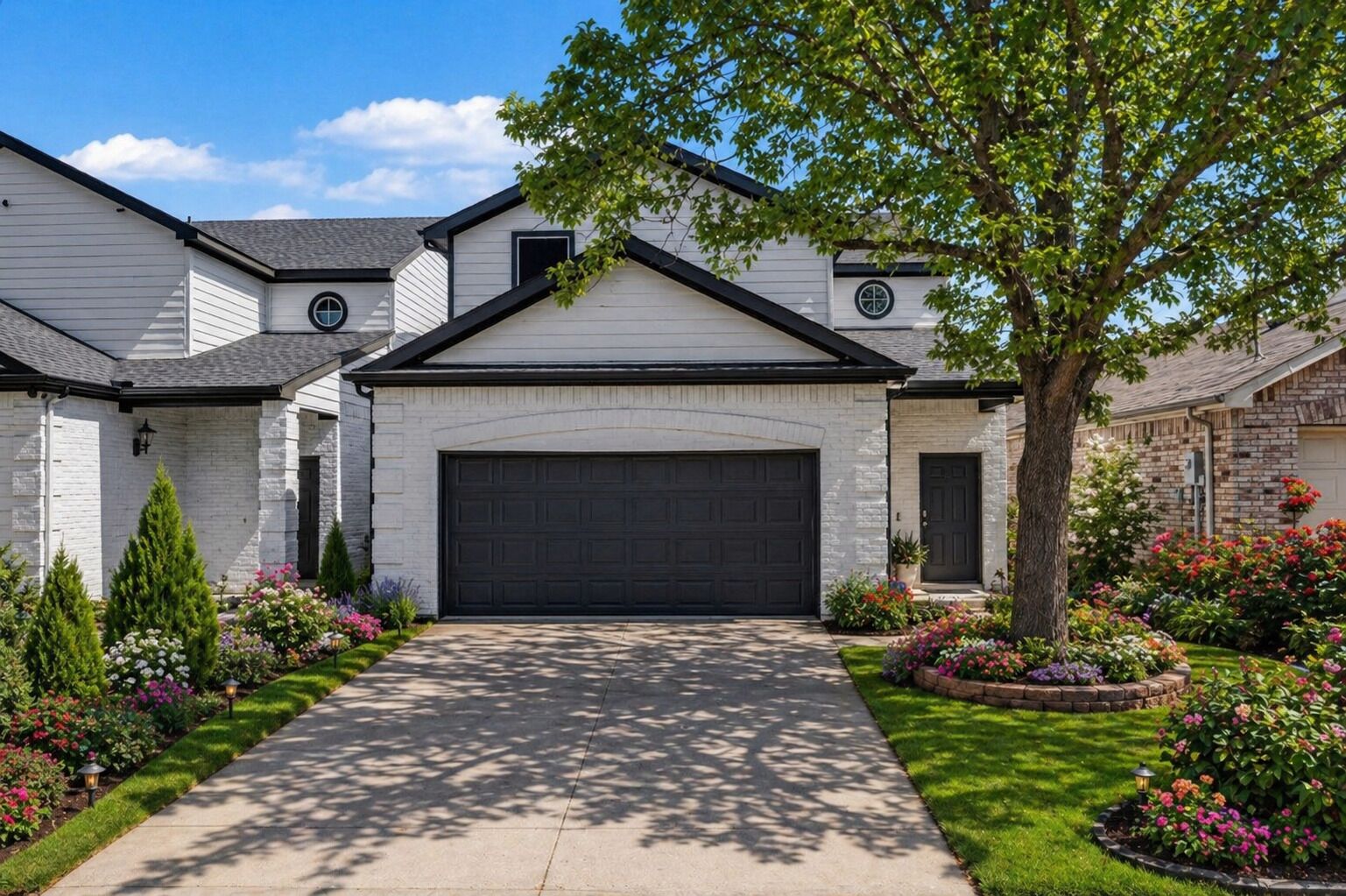 A residential house with a garage, a well-maintained lawn, and a variety of flowering plants.