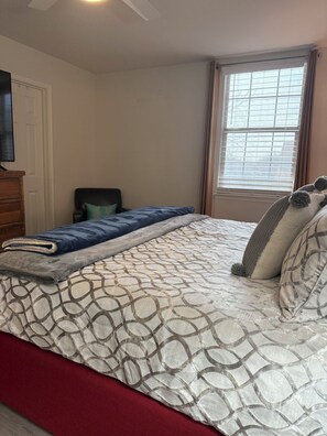 Ein Schlafzimmer mit einem Bett, einem Sessel, einem Fernseher und einem Fenster.