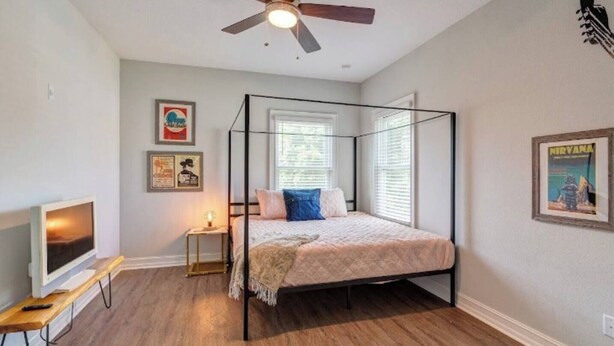 Ein Schlafzimmer mit Himmelbett, Deckenventilator, Fernseher auf einem Schrank und gerahmten Bildern an der Wand.