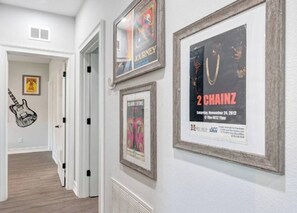 A hallway with framed posters on the wall, a door, and a guitar wall art piece. - ♫Rock n’ Roll Bungalow♫Balcony☞3 King Beds ☜ (Tampa)