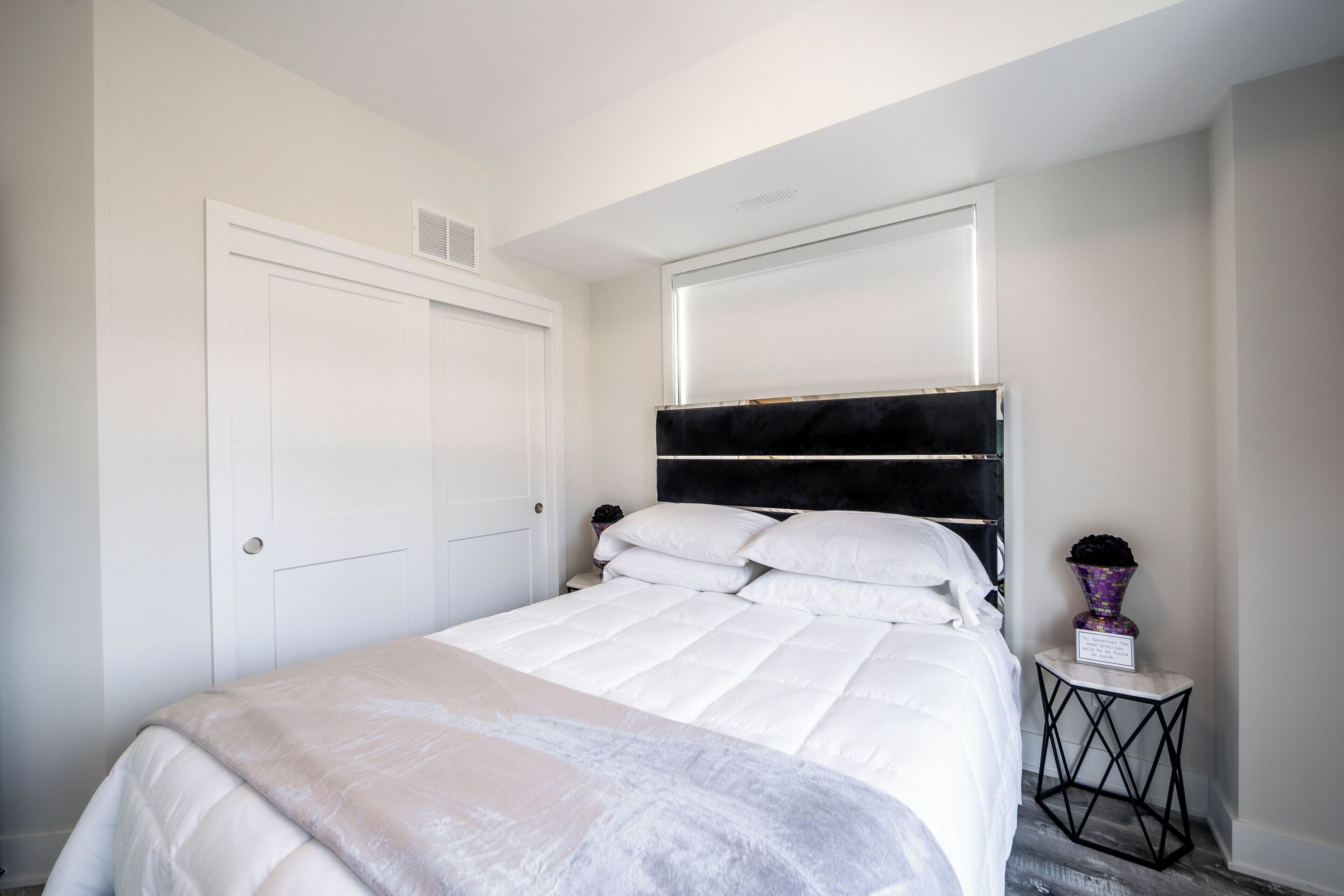 A neatly made bed with white bedding and a headboard with a black panel.