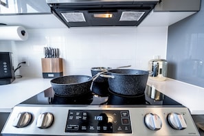 Una cocina con una campana extractora de acero inoxidable, un reloj digital que marca las 11:59 y un juego de utensilios de cocina negros sobre la estufa.