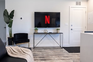 A modern living room with a black sofa, a TV with a red 'N' logo, a console table with decorative items, and a door.