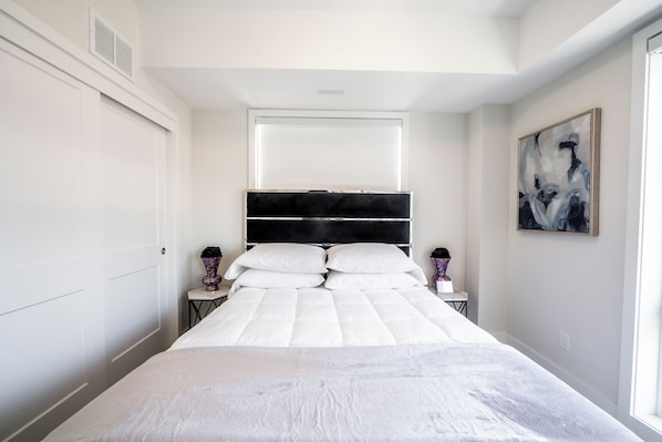 Un dormitorio moderno con una cama grande, cabecera, mesitas de noche y un cuadro en la pared.