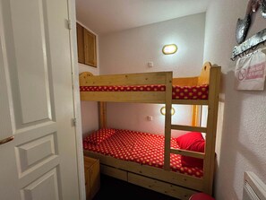 Uma cama de beliche com colchão estampado vermelho, cabeceira de madeira e uma pequena janela com luminária.