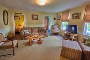 A cozy living room with a sofa, armchair, ottoman, and a coffee table. - Cozy 4 Bedroom house across from Crystal Lake. " The Crooked Old House " (Barton)