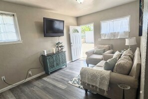Ein Wohnzimmer mit einem beigefarbenen Sofa, einem an der Wand befestigten Fernseher und einer zur Außenseite führenden Tür.