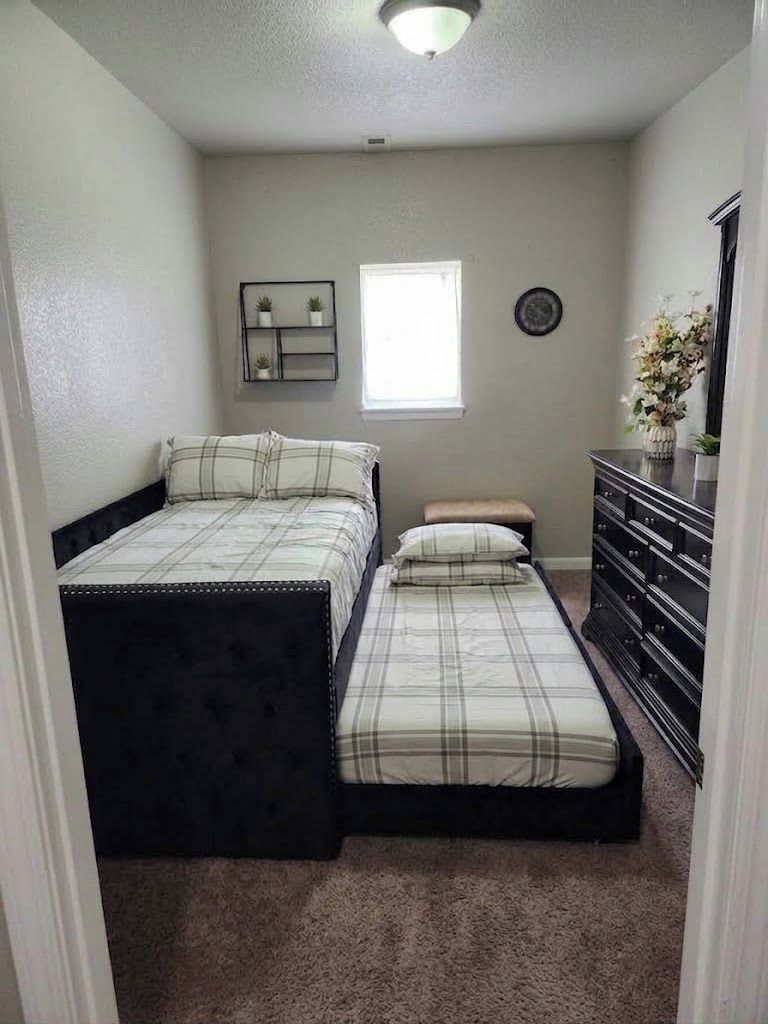 Un dormitorio con cama doble, mesita de noche, cómoda, ventana y estante en la pared.