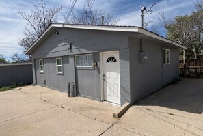 Ein eingeschossiges Gebäude mit einer Garagentür, einem kleinen Anbau und einem umzäunten Garten.